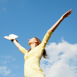 Young woman staying with raised hands against blue sky